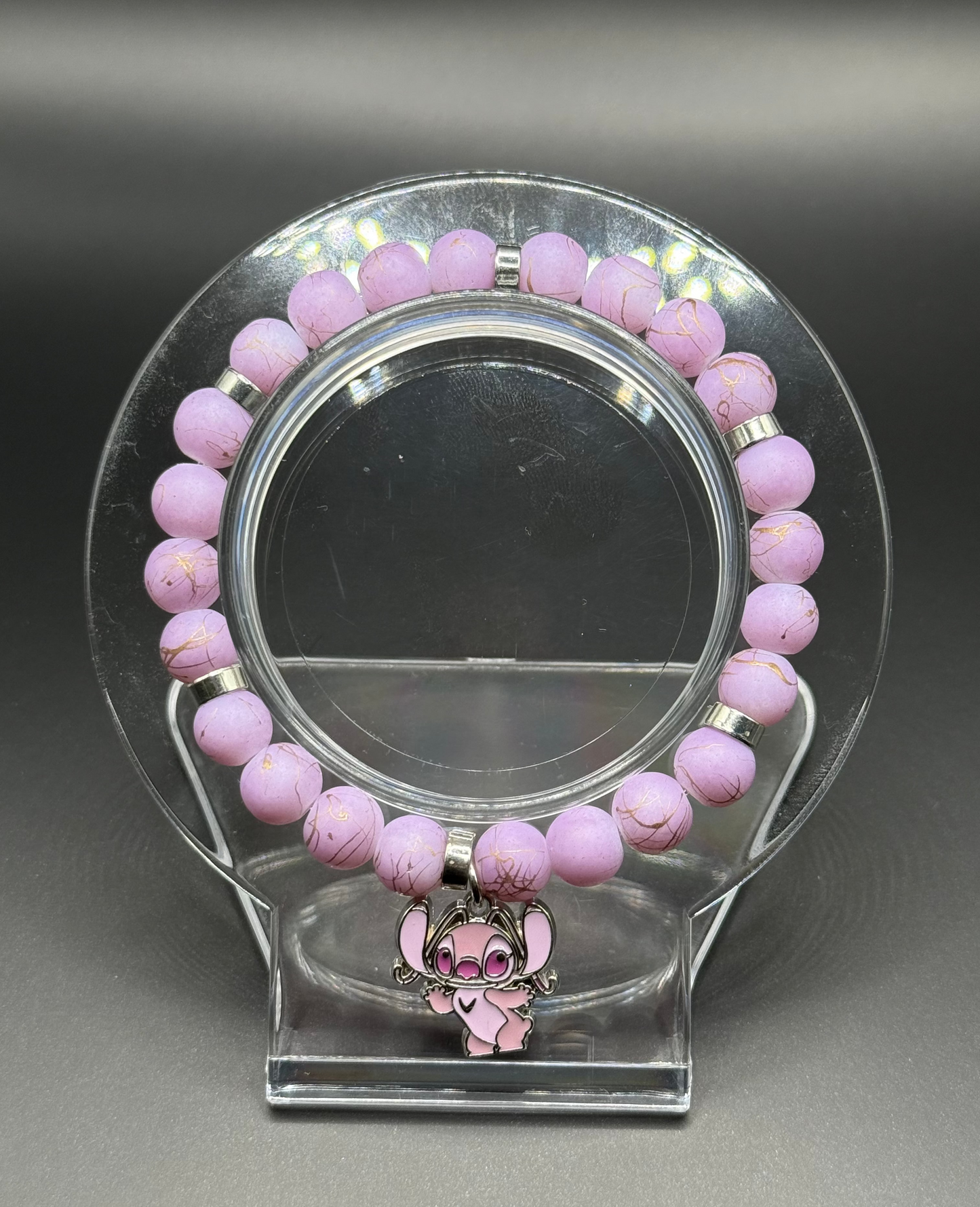 Pink beaded bracelet with a pink Angel (Lilo & Stitch) charm on a clear stand against a gray background