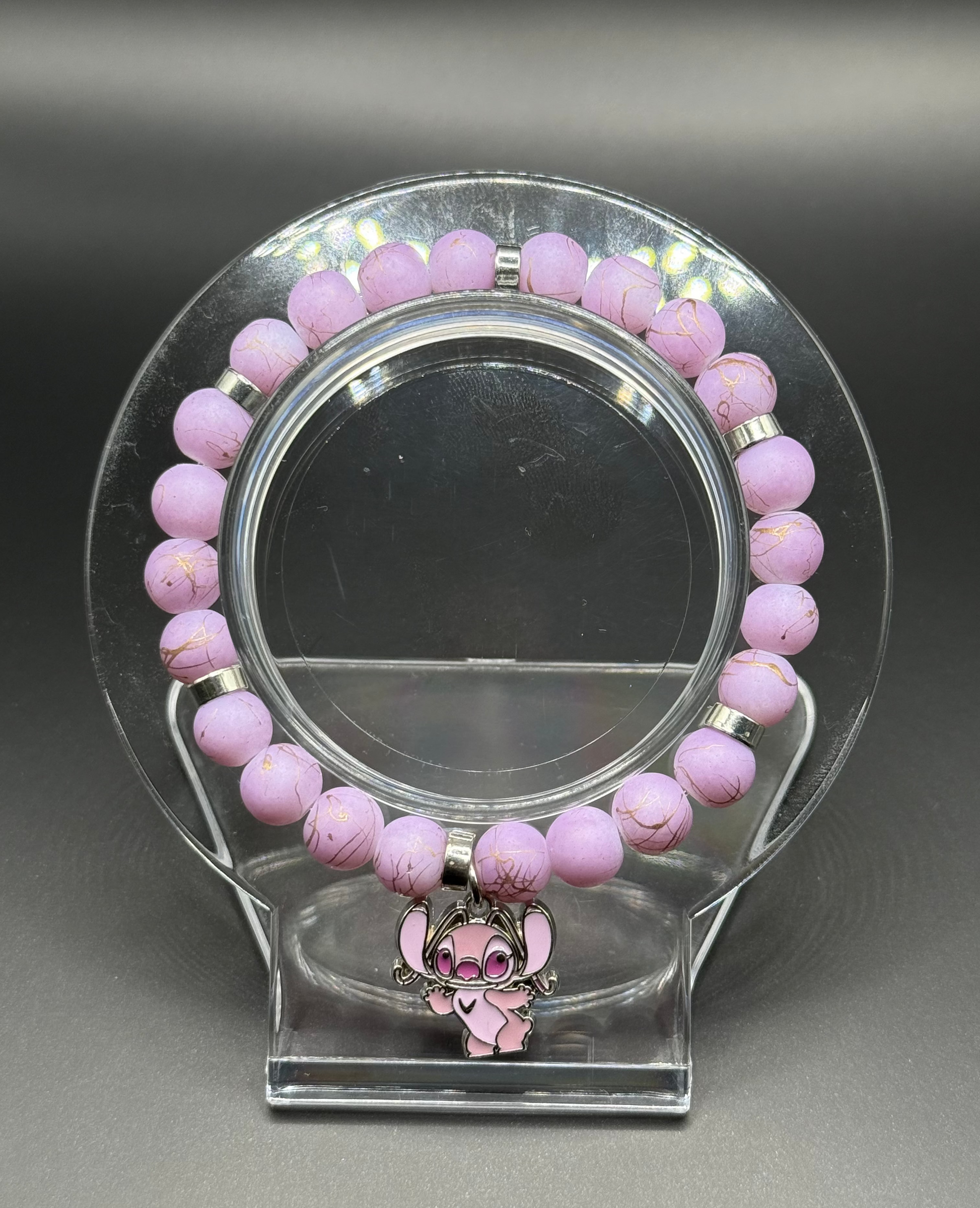 Pink beaded bracelet with a pink Angel (Lilo & Stitch) charm on a clear stand against a gray background