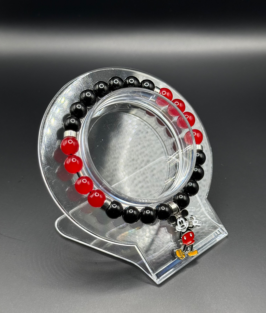 Black and red beaded bracelet with a character charm on a clear stand against a dark background