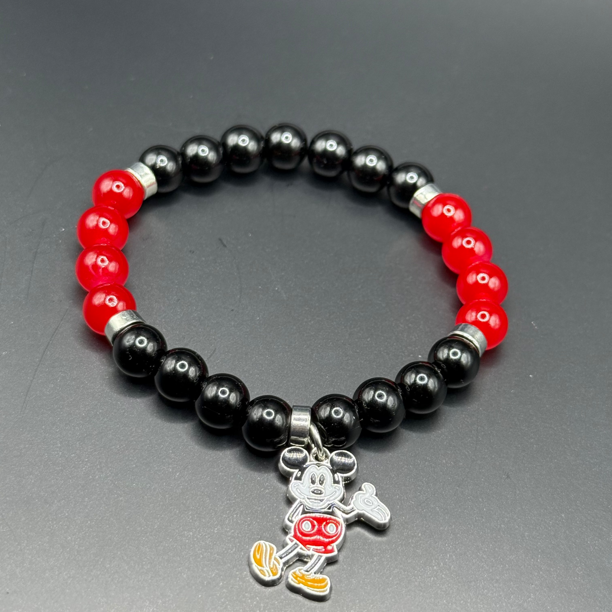 Bracelet with black and red beads and a Mickey Mouse charm on a gray background