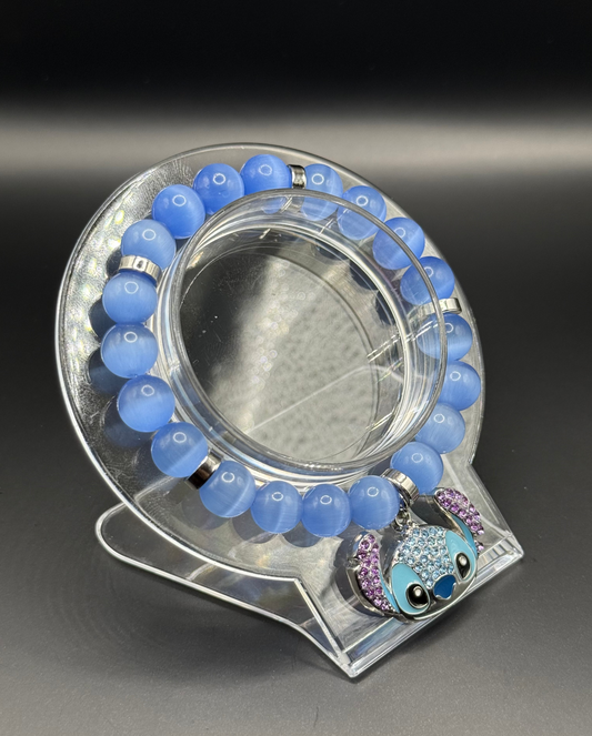 Blue beaded bracelet with a decorative Stitch (Lilo & Stitch) charm on a clear stand against a dark background